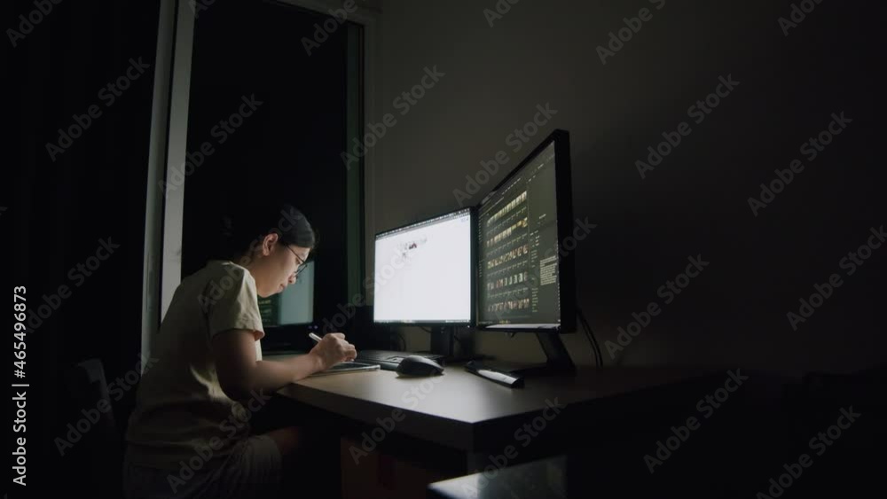 A young woman writes an article on a tablet at night in a home office, scrolling news feeds, and searching data of online information for her work plan. A young woman writes an article on a tablet at night in a home office, scrolling news feeds, and searching data of online information for her work plan.
