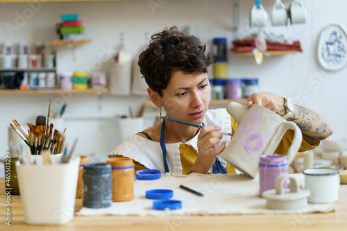 Young creative woman small business owner work in art studio with pottery for handmade shop. Girl relax with painting, ceramics after work create craft kitchenware in workshop. Artistic hobby concept photo