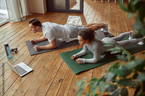 Top view of athletic man and woman in plank position in front of notebook during workout