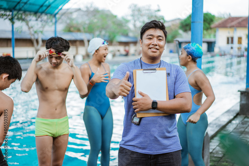 a swimming trainer smiling with thumbs up while holding a clipboard