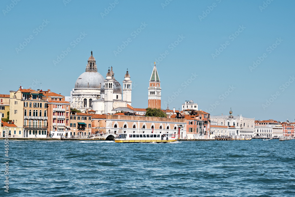 Old buildings on Dorsodouro promenade, cupola of Santa Maria della Salute church, St Mark's Campanile tower in Venice, Italy. Traditional Venetian architecture and passenger boat, view from lagoon.