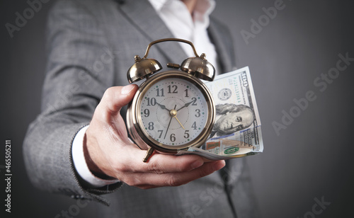 Businessman holding alarm clock and dollar banknotes.