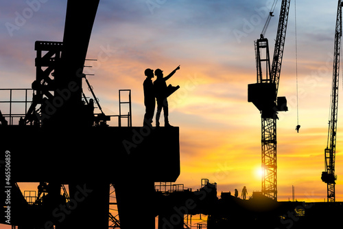 Фотография Silhouette of Engineer and worker checking project at heavy infrastructure building site background, construction site at sunset in evening time