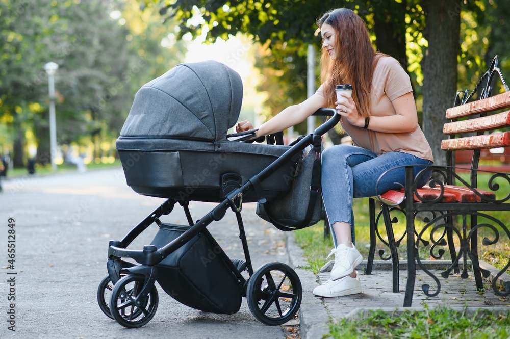 Happy young mother with baby in buggy sitting on bench in autumn park