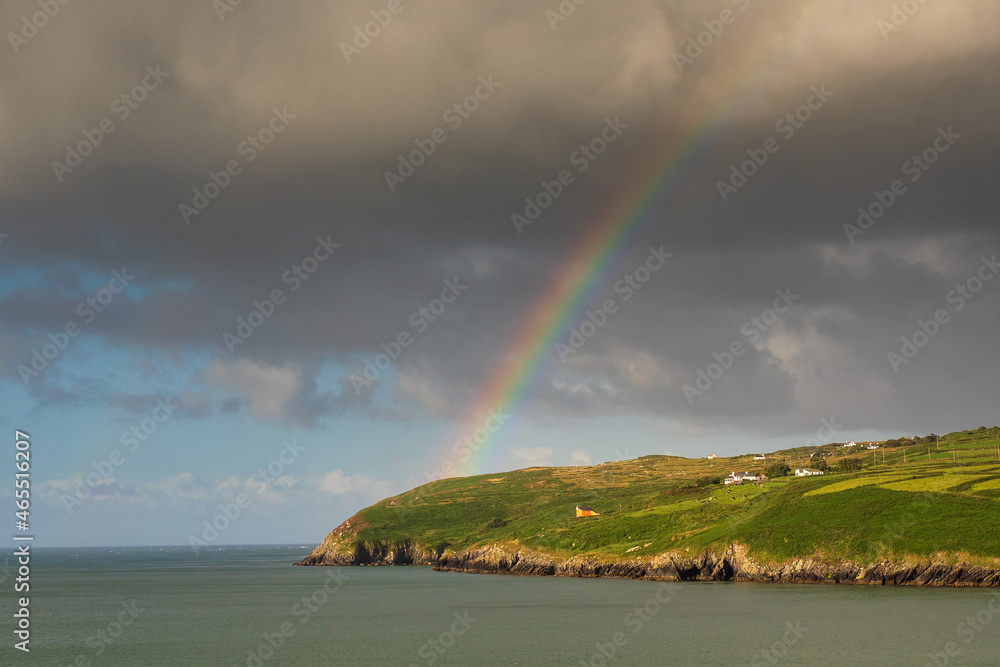 View on Mizen Peninsula in county Cork, Ireland. Colorful rainbow symbol of luck in the sky. Calm water of Atlantic ocean and green fields. Irish landscape. Popular travel destination. Nature wonder.