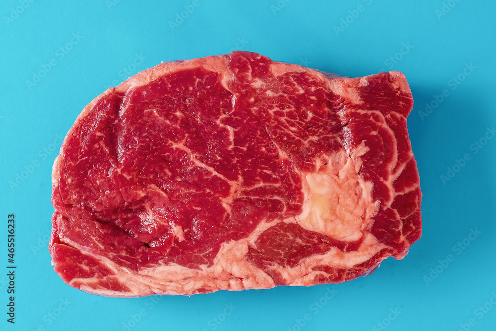 Obraz premium Fresh juicy rib eye steak on blue surface. Top quality fresh meat. Butcher craft product and meat industry. Rich red color and marbling. Premium cut.