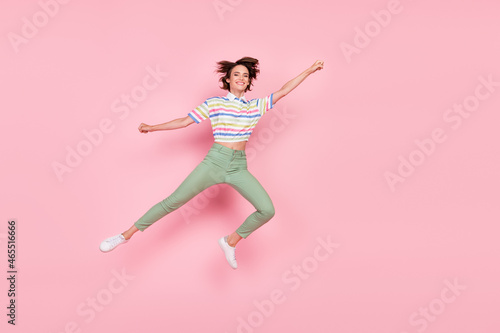 Full body photo of young girl happy positive smile fly air superwoman catch parasol jump isolated over pink color background