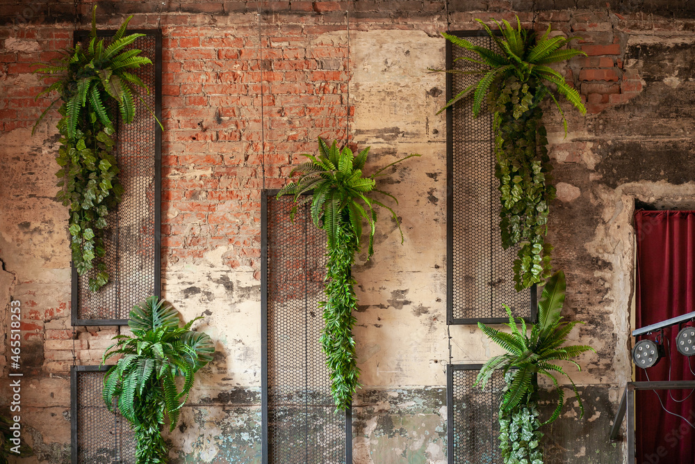 Artificial plants fern and ivy hang on an old ruined brick wall with a lattice