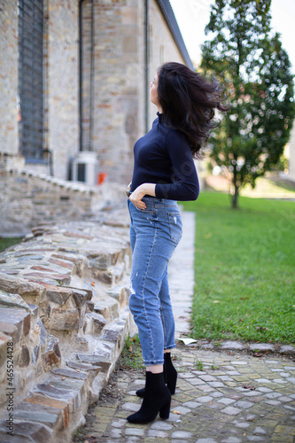 Young white girl with dark hair in jeans outside looking at old stone building