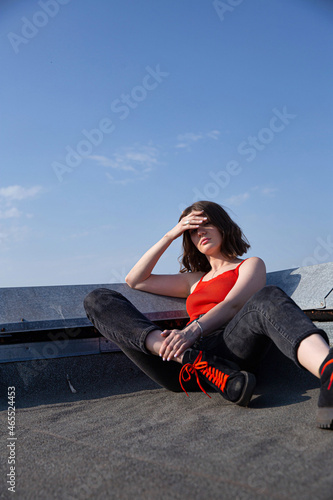 Young white european woman with dark hair on the roof with clear sky behind covering her face by hand