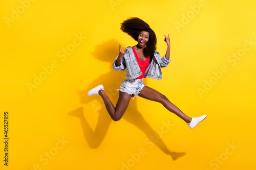 Fototapeta Naklejka Na Ścianę i Meble -  Full length body size photo of girl jumping showing heavy metal sign laughing isolated bright yellow color background
