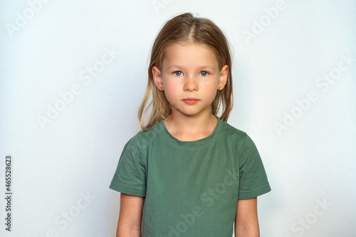serious child looks at the camera. place for text. Portrait of a girl on a white background. Collected hair and green T-shirt. Cute smile happy smile. A cheerful preschool 