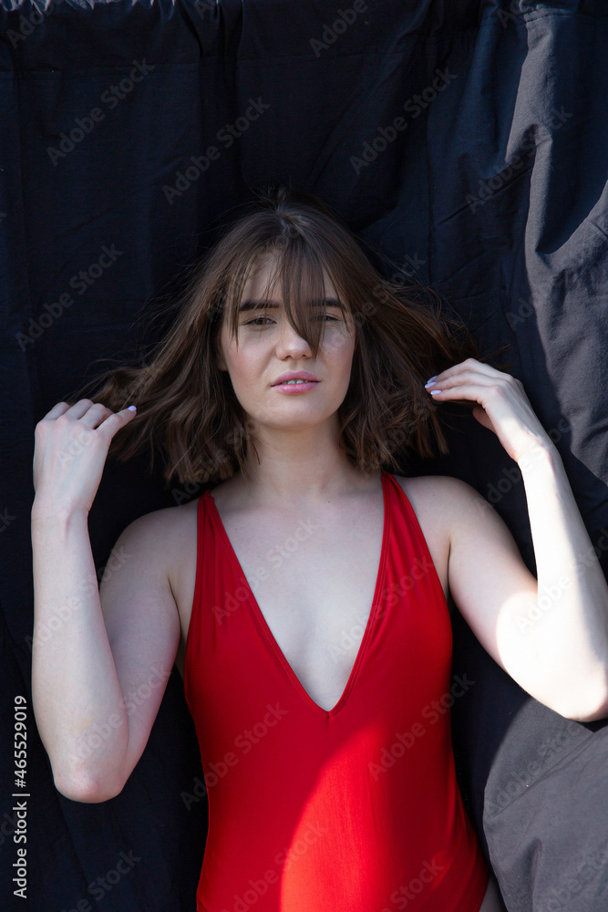 Fototapeta premium Young caucasian woman in red swimsuit near black cloth
