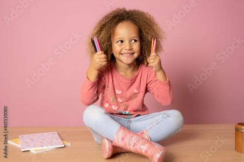 Beautiful little girl holding multicolor crayons set in art school children education concept isolated over pink background