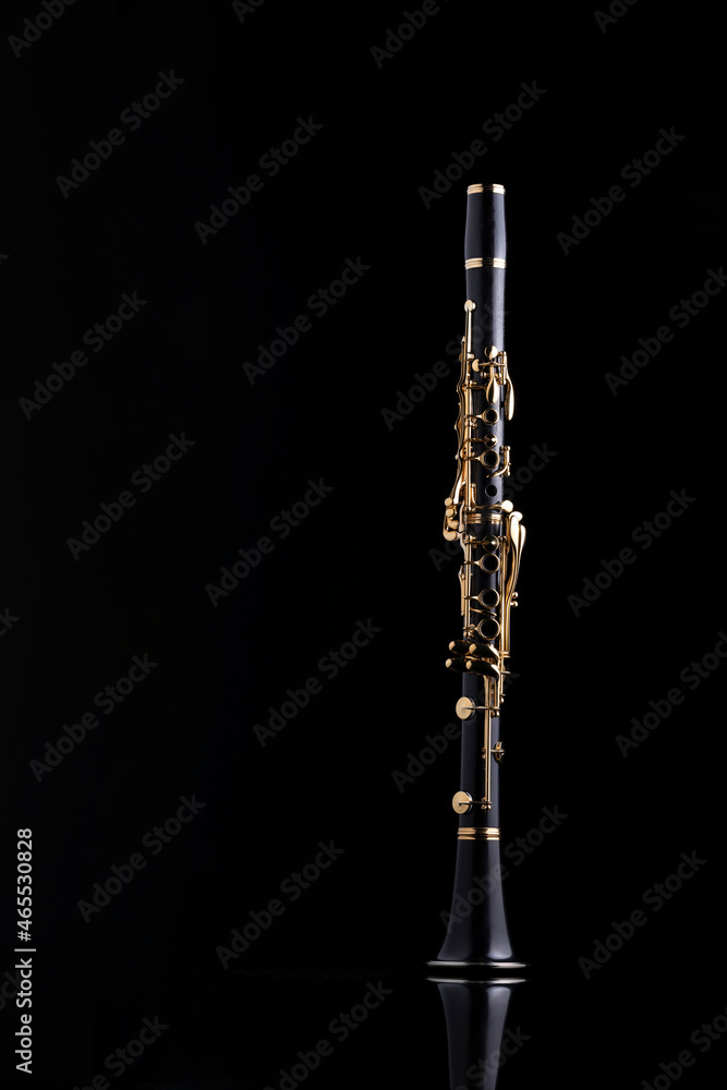A full size clarinet with gold plated keys on a reflective surface and a black background. A woodwind instrument common to classical music. A full size clarinet with gold plated keys on a reflective surface and a black background. A woodwind instrument common to classical music.