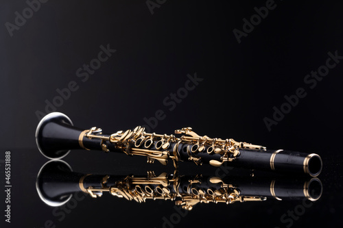 Slika na platnu A full size clarinet with gold plated keys laying on a reflective surface with a dark background