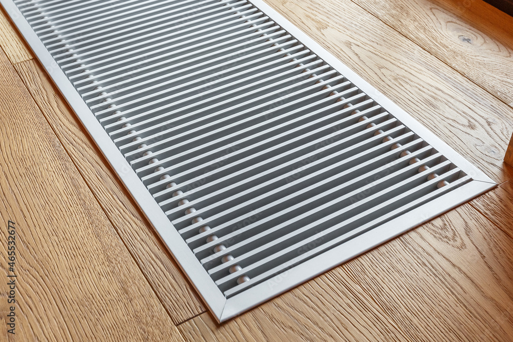Metal grill of a modern convector heating in the floor next to the window. Selective focusing. Metal grill of a modern convector heating in the floor next to the window. Selective focusing.