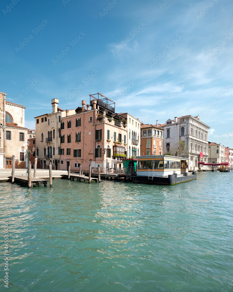 Grand Canal in Venice, Italy. Passenger vaporetto boat station and historic buildings on green water with blue sky. Venice water transport system. Water taxi system, logos removed for commercial use.