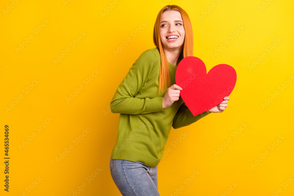 Photo of funky red hairdo young lady hold heart look empty space wear green sweater isolated on yellow color background Photo of funky red hairdo young lady hold heart look empty space wear green sweater isolated on yellow color background