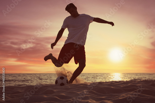Man playing football on beach at sunset