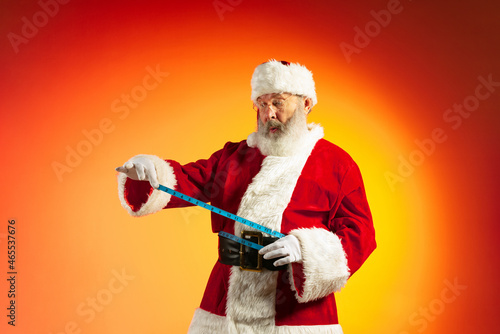 Emotional senior man, Santa Claus posing isolated on red yellow background in neon. Healthy New Year 2022