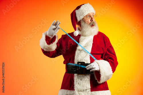 Emotional senior man, Santa Claus posing isolated on red yellow background in neon. Healthy New Year 2022