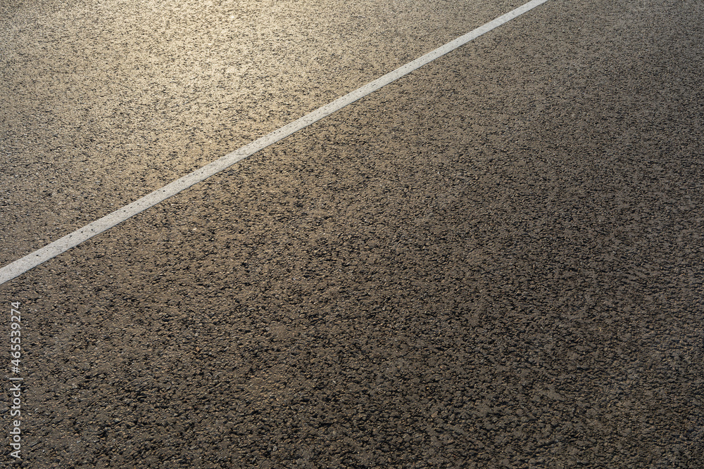 The texture of a new asphalt road with a dividing white stripe on a sunny morning