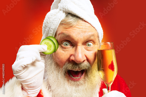 Close-up funny senior man wearing white towl and costume of Santa Claus congrats everybody with New Year 2022 photo