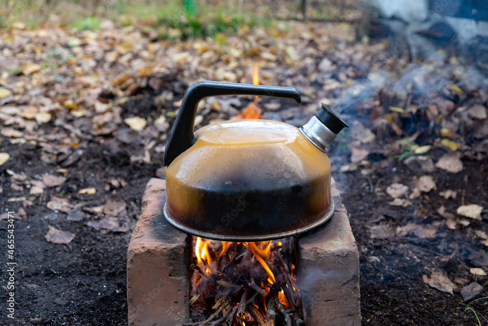 Smoked metal kettle boils on fire on bricks outdoors Smoked metal kettle boils on fire on bricks outdoors