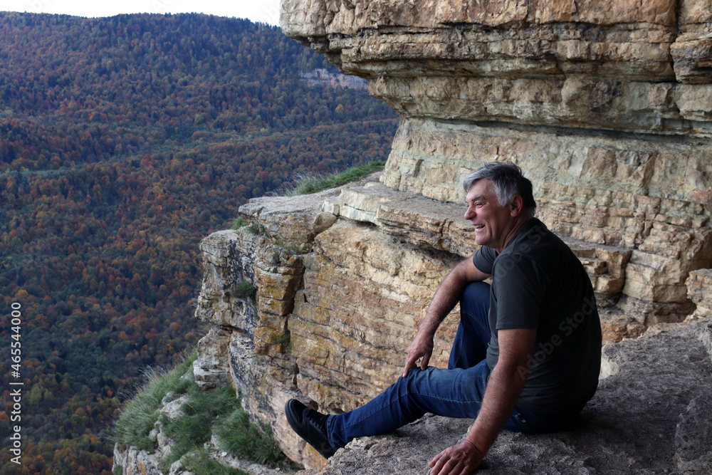 A man sits on the edge of a cliff and looks at the misty valley and the autumn forest.