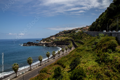 beautiful coastal road in madeira with palm trees and a beach with black stones