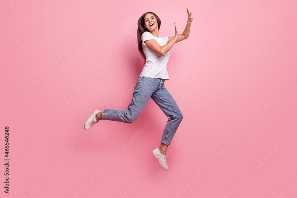 Full size profile photo of impressed young brunette lady jump wear t-shirt jeans sneakers isolated on pink background