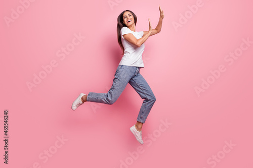 Full size profile photo of impressed young brunette lady jump wear t-shirt jeans sneakers isolated on pink background