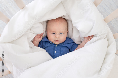 baby boy in a blanket in a crib, happy newborn wakes up in the morning or goes to bed