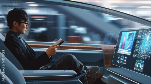Futuristic Concept: Handsome Stylish Japanese Businessman in Glasses Reading Notebook and Watching News on Augmented Reality Screen while Sitting in a Autonomous Self-Driving Zero-Emissions Car.  photo