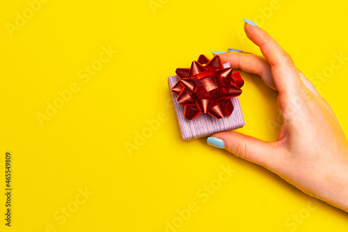 Hand with a gift box on yellow background with free space for text, list of presents for boxing day on Christmas eve.