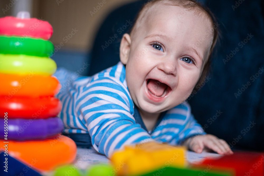 A little kid in a striped suit is lying on his tummy, next to him a children's pyramid and toys. High quality photo A little kid in a striped suit is lying on his tummy, next to him a children's pyramid and toys. High quality photo