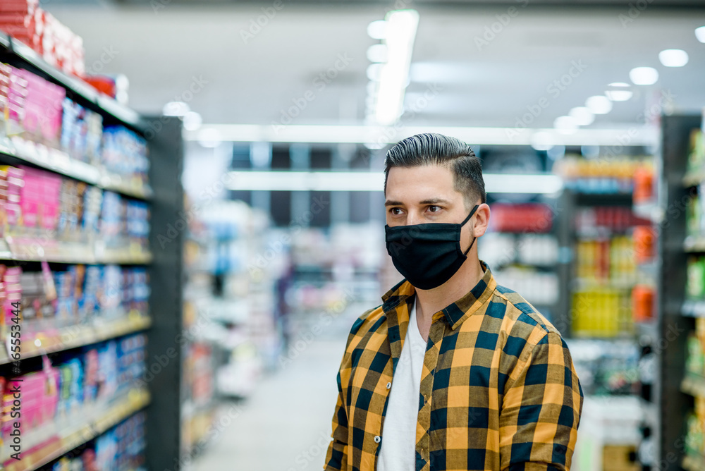 Young handsome man in a supermarket wearing protective mask while grocery shopping