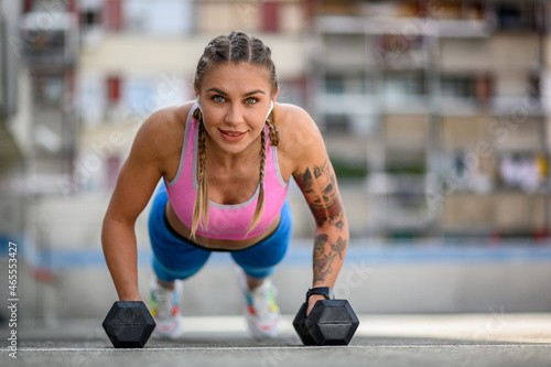 Woman training outside while using dumbbells and airpods
