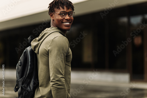 Happy successful african student, wearing glasses and with a black backpack, standing on the steps and smiling © Shopping King Louie