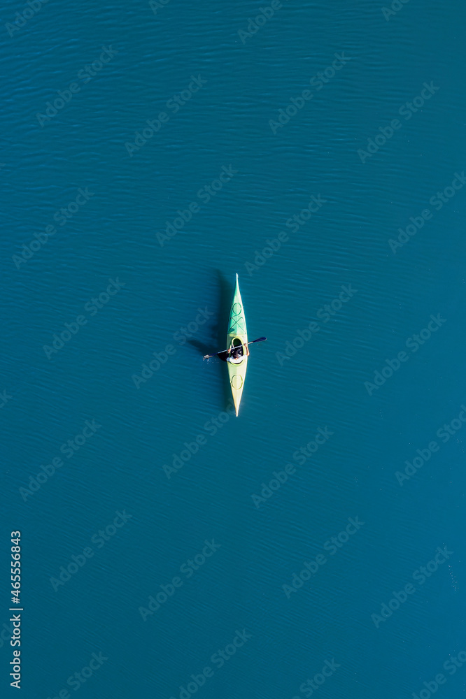 View from above, aerial view of a person paddling a canoe - kayak on the Cedrino Lake surrounded by the mountain range of Supramonte located northeast of the Gennargentu massif. Sardinia, Italy.