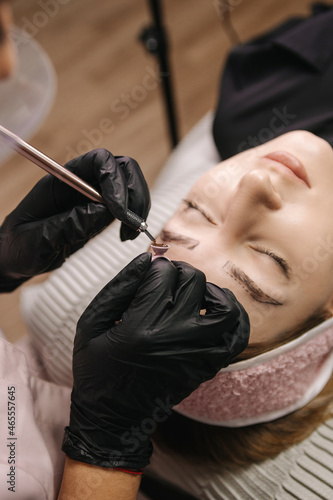 The hand of the master in a black glove holds the handpiece with the needle and collects the paint pigment in the ring before microblading.