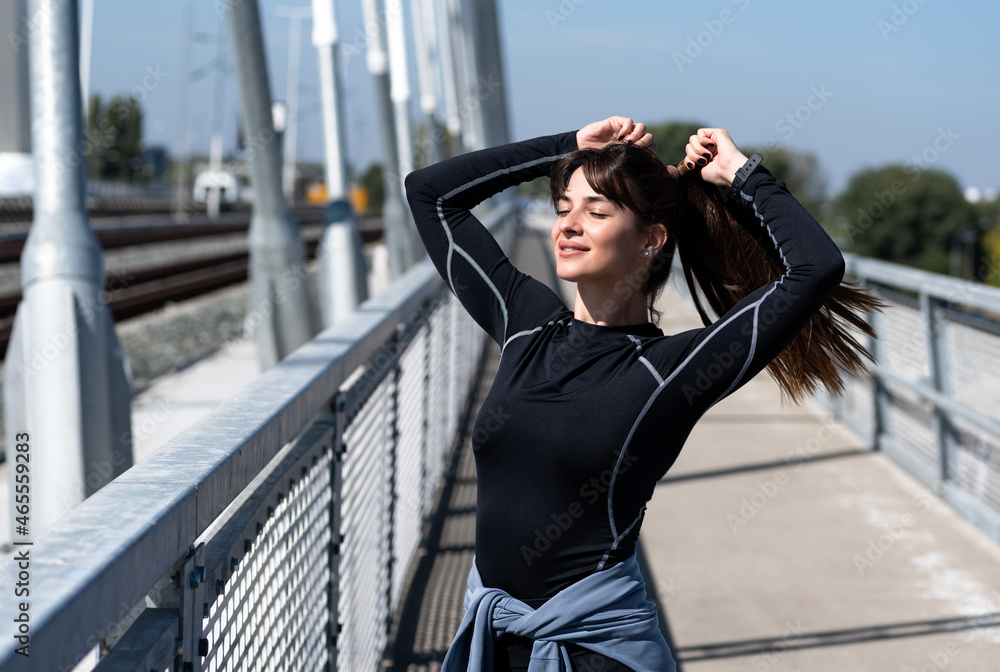 Young sporty runner fitness woman tying her hair before her everyday morning run workout on a sunny autumn day. Urban jogging sport concept. Young sporty runner fitness woman tying her hair before her everyday morning run workout on a sunny autumn day. Urban jogging sport concept.