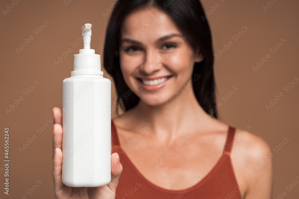 Guilty pleasure. Cropped view of a perfect female holding cream or lotion at her hand and stretching it to the camera. Focus at the bottle Guilty pleasure. Cropped view of a perfect female holding cream or lotion at her hand and stretching it to the camera. Focus at the bottle