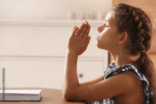 Photography Cute little girl praying over Bible at table in room