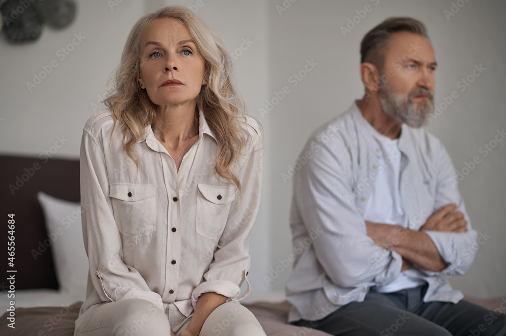 Unhappy mature couple sitting apart in silence Unhappy mature couple sitting apart in silence