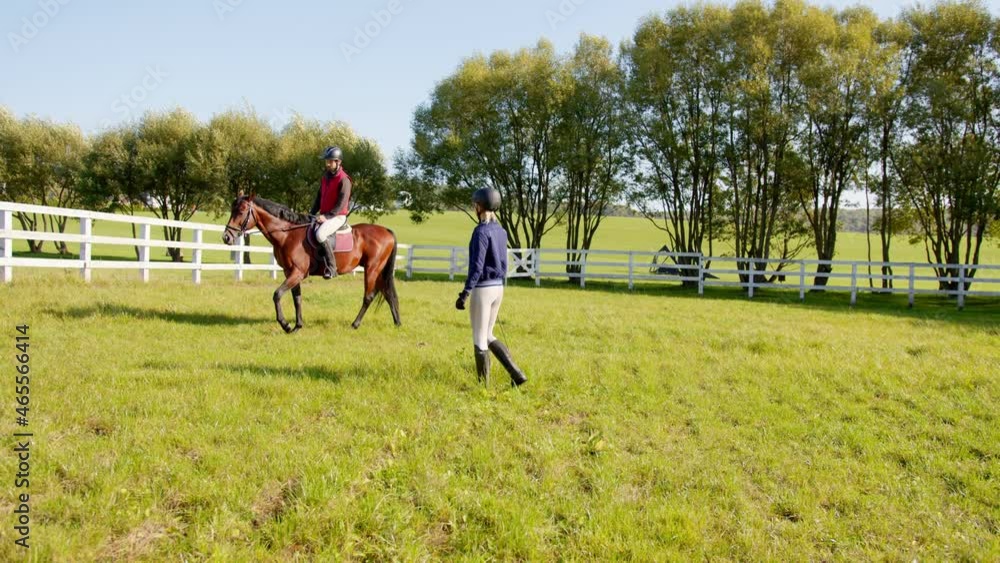 During training. Full length view of the caucasian jokey woman looking at the man sitting at the horse and holding training during the summer During training. Full length view of the caucasian jokey woman looking at the man sitting at the horse and holding training during the summer