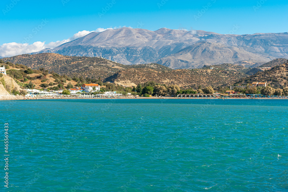 Wind-protected beach and bay with sun loungers and umbrellas in the popular tourist resort of Agia Galini in the south of Crete. In the background the IDA mountain range with the mighty Psiloritis
