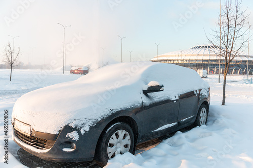The car in the parking lot is covered with snow. Car under the snow. Consequences of heavy snowfall. Concept of snowy weather, snowfall, bad winter weather conditions, the effects of a blizzard.