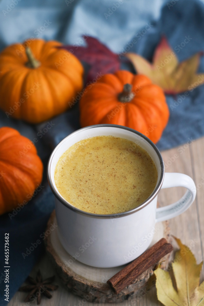 A cup of healthy pumkin spices latte with butter and a cinnamon and fall leaves with small squash and fall red leaves in background. An ideal warming fall drink and for diet. A cup of healthy pumkin spices latte with butter and a cinnamon and fall leaves with small squash and fall red leaves in background. An ideal warming fall drink and for diet.